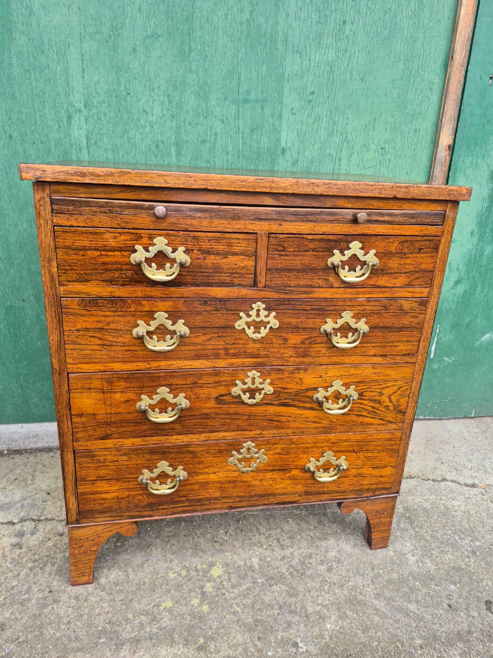 A small rosewood chest of drawers featuring brass handles, bracket feet, and a pull-out brushing slide. View X