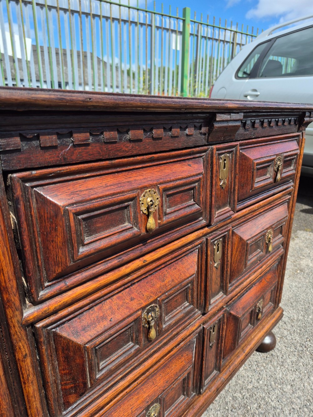 A dark oak chest of drawers featuring three drawers with geometric panel mouldings, brass drop handles, and turned bun feet. View V