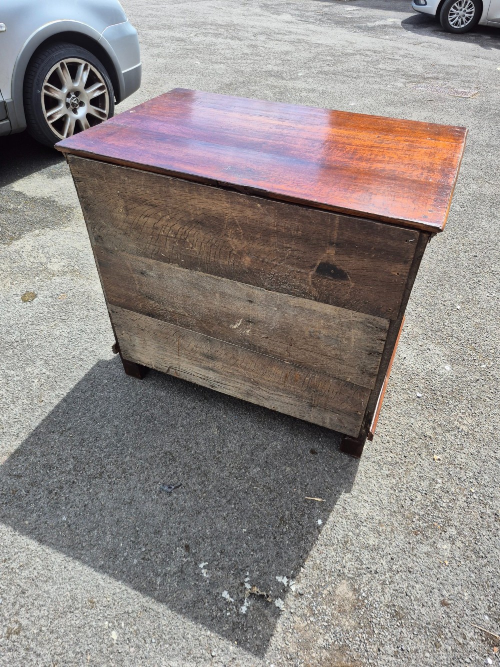 A dark oak chest of drawers featuring three drawers with geometric panel mouldings, brass drop handles, and turned bun feet. View VI