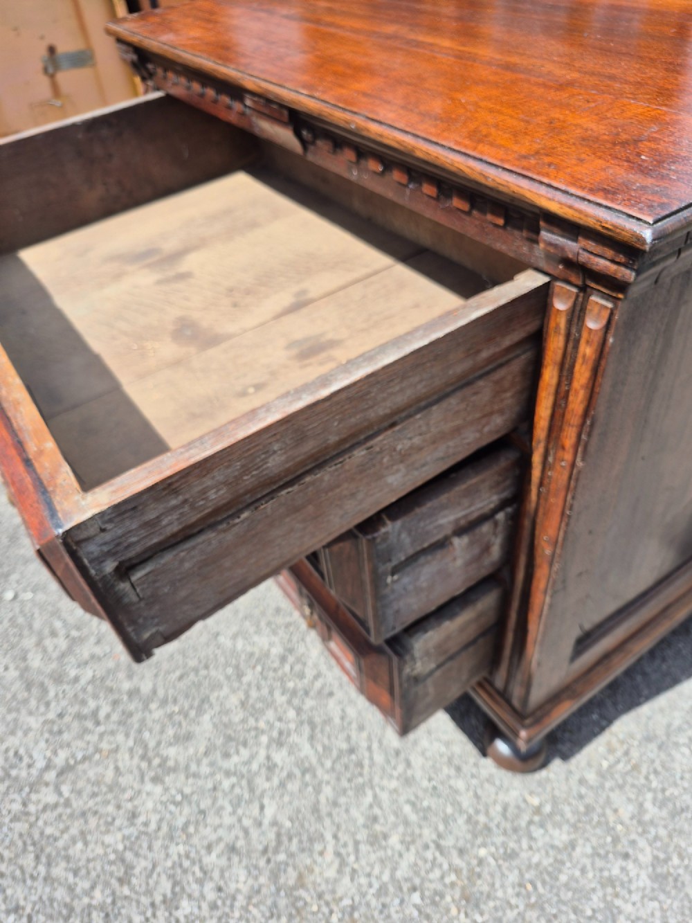 A dark oak chest of drawers featuring three drawers with geometric panel mouldings, brass drop handles, and turned bun feet. View VII