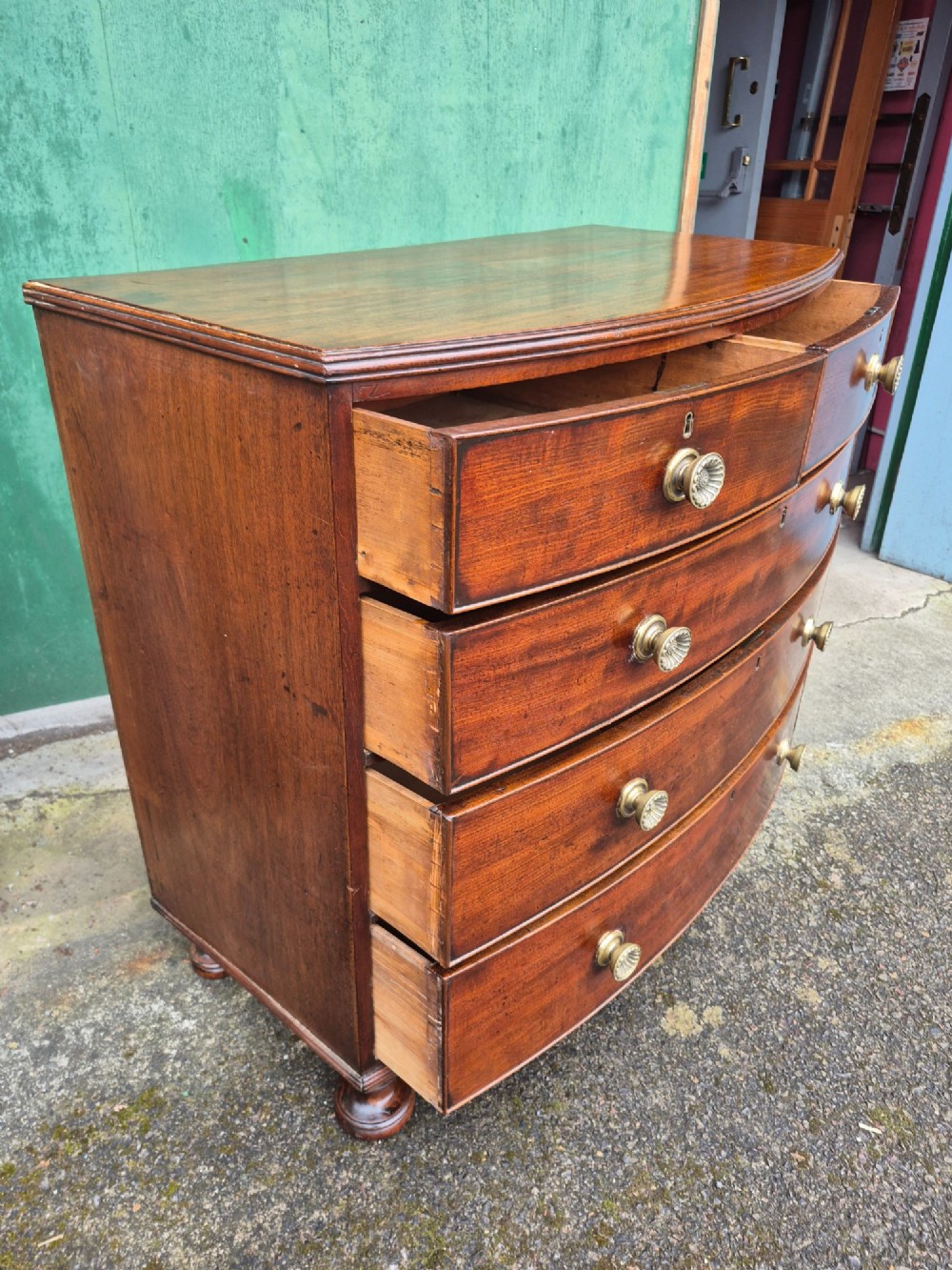 An antique mahogany bowfront chest of drawers featuring two short drawers over three long drawers with brass rosette knobs and turned feet. View V