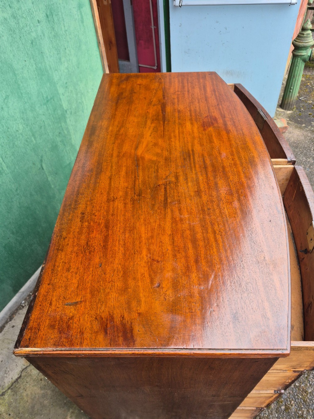An antique mahogany bowfront chest of drawers featuring two short drawers over three long drawers with brass rosette knobs and turned feet. View VIII
