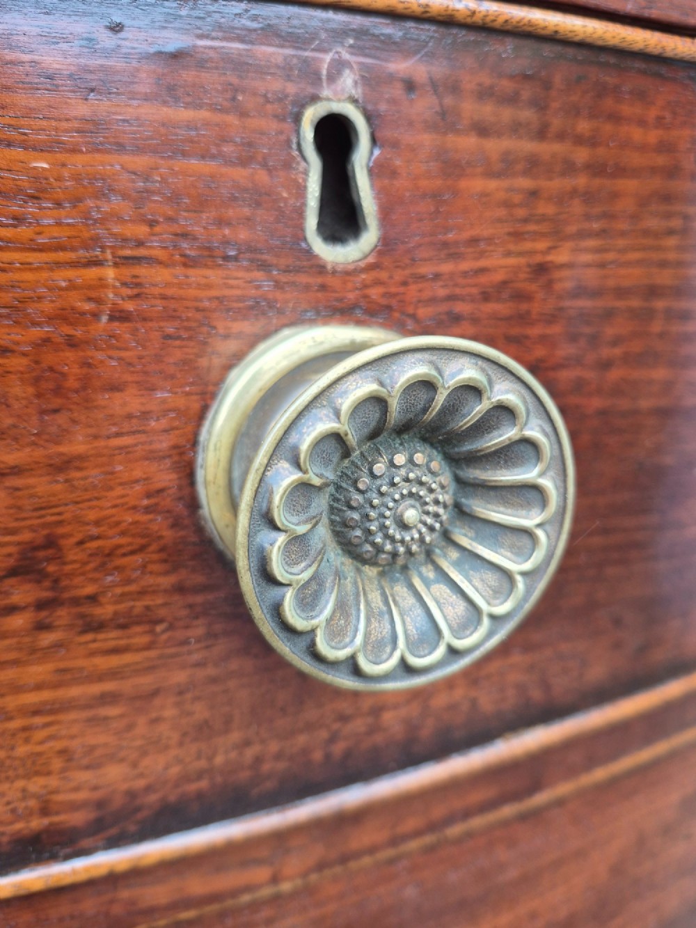 An antique mahogany bowfront chest of drawers featuring two short drawers over three long drawers with brass rosette knobs and turned feet. View IX