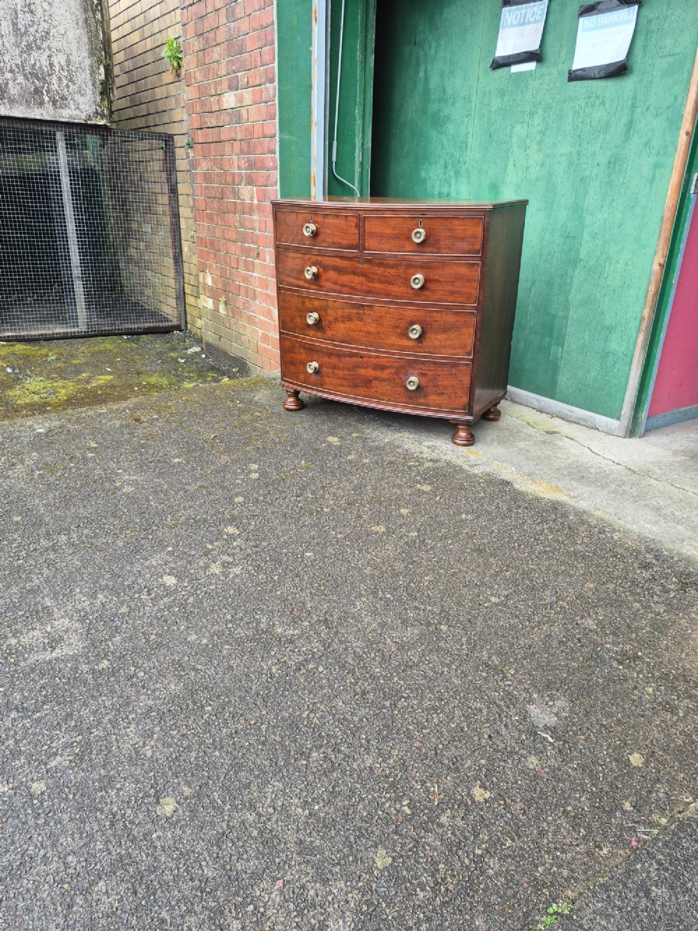 An antique mahogany bowfront chest of drawers featuring two short drawers over three long drawers with brass rosette knobs and turned feet. View X