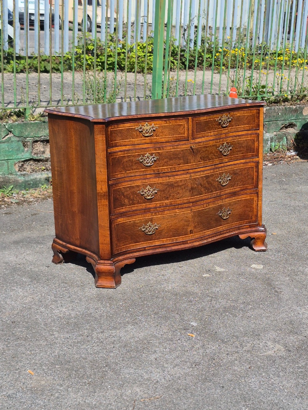 A burr walnut serpentine-front chest of drawers with two short top drawers over three long drawers, featuring brass backplate handles and resting on bracket feet. View II
