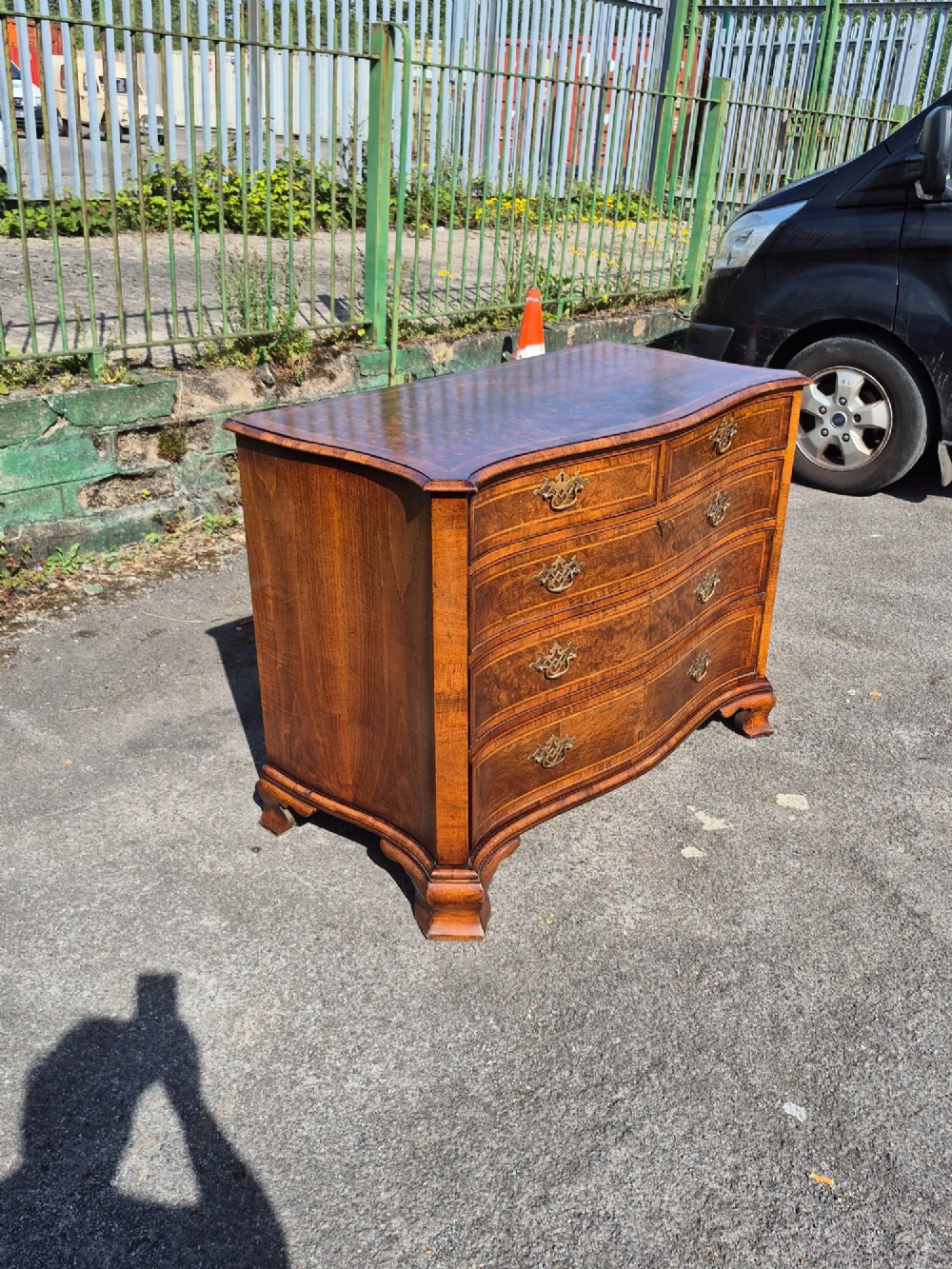 A burr walnut serpentine-front chest of drawers with two short top drawers over three long drawers, featuring brass backplate handles and resting on bracket feet. View III