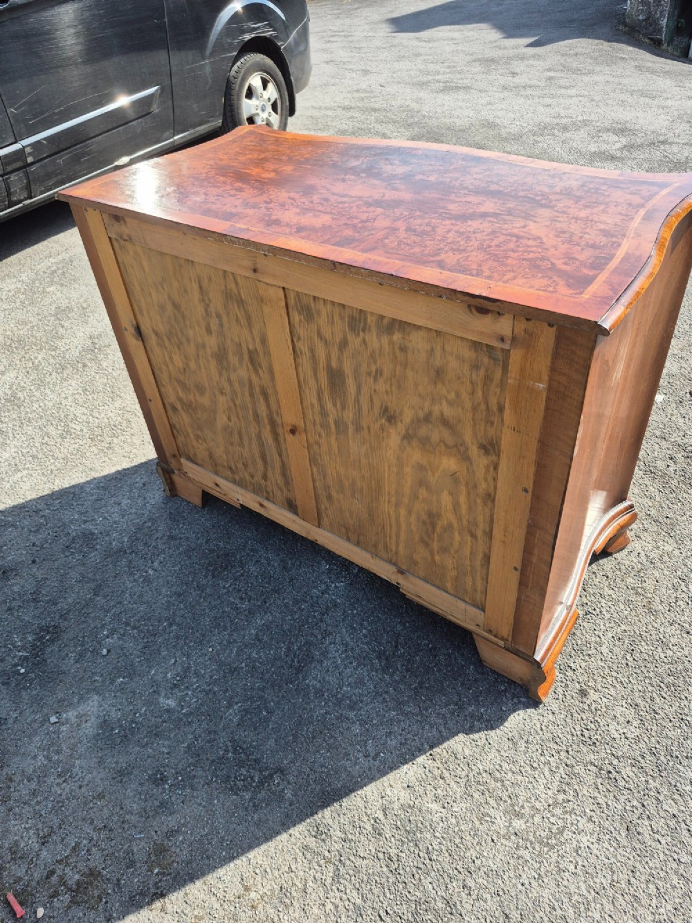 A burr walnut serpentine-front chest of drawers with two short top drawers over three long drawers, featuring brass backplate handles and resting on bracket feet. View VI