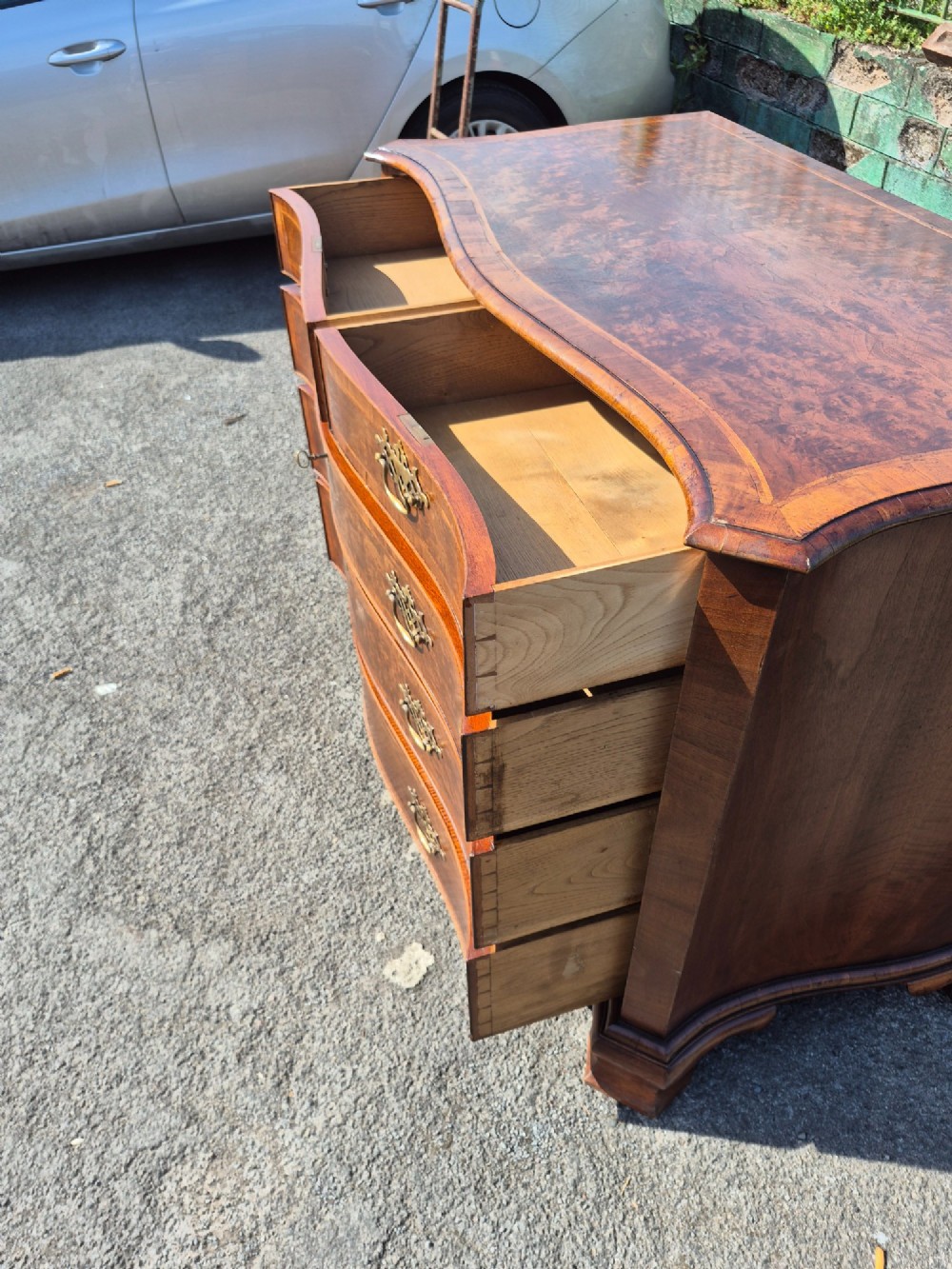 A burr walnut serpentine-front chest of drawers with two short top drawers over three long drawers, featuring brass backplate handles and resting on bracket feet. View VIII