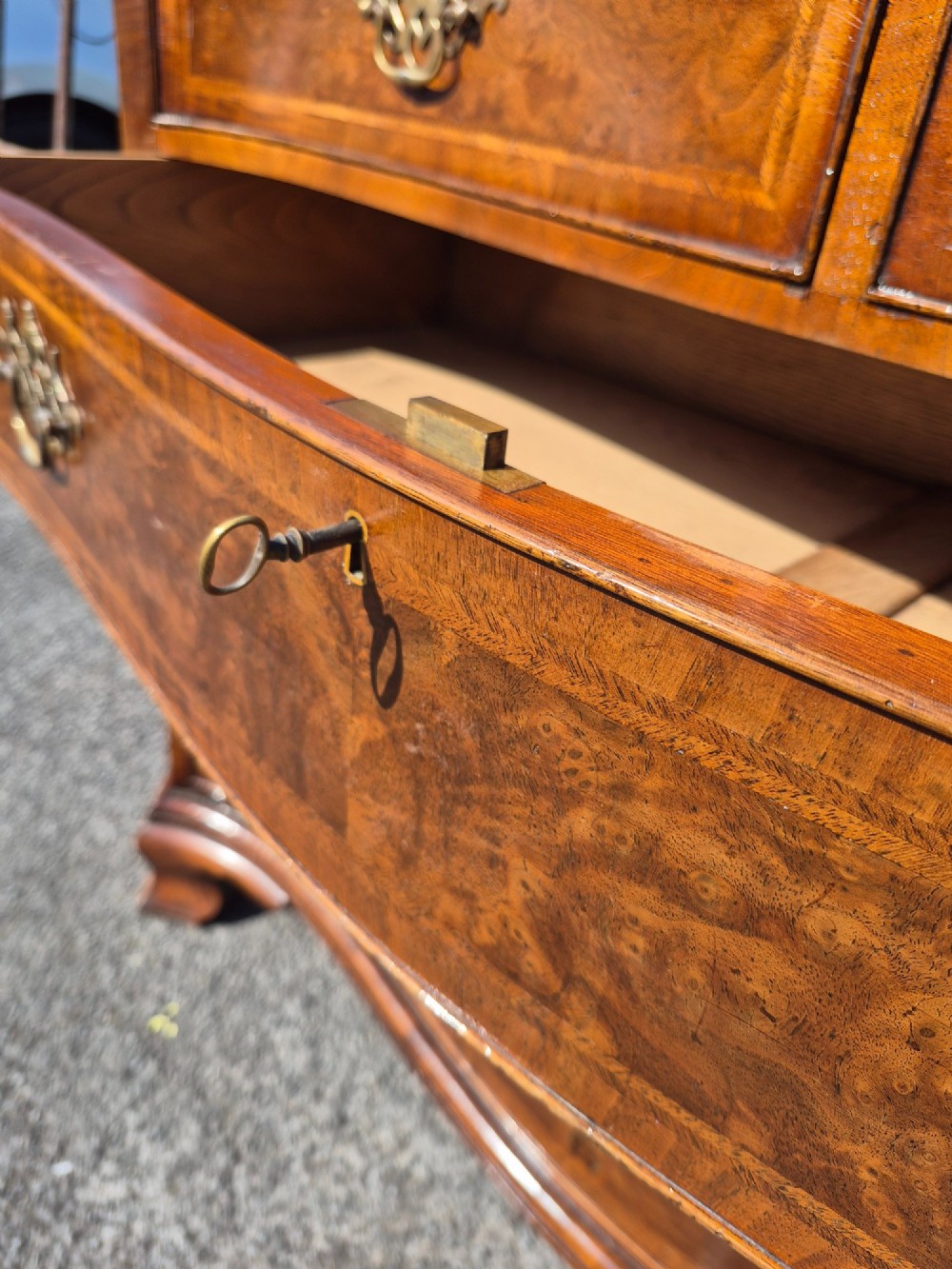 A burr walnut serpentine-front chest of drawers with two short top drawers over three long drawers, featuring brass backplate handles and resting on bracket feet. View IX