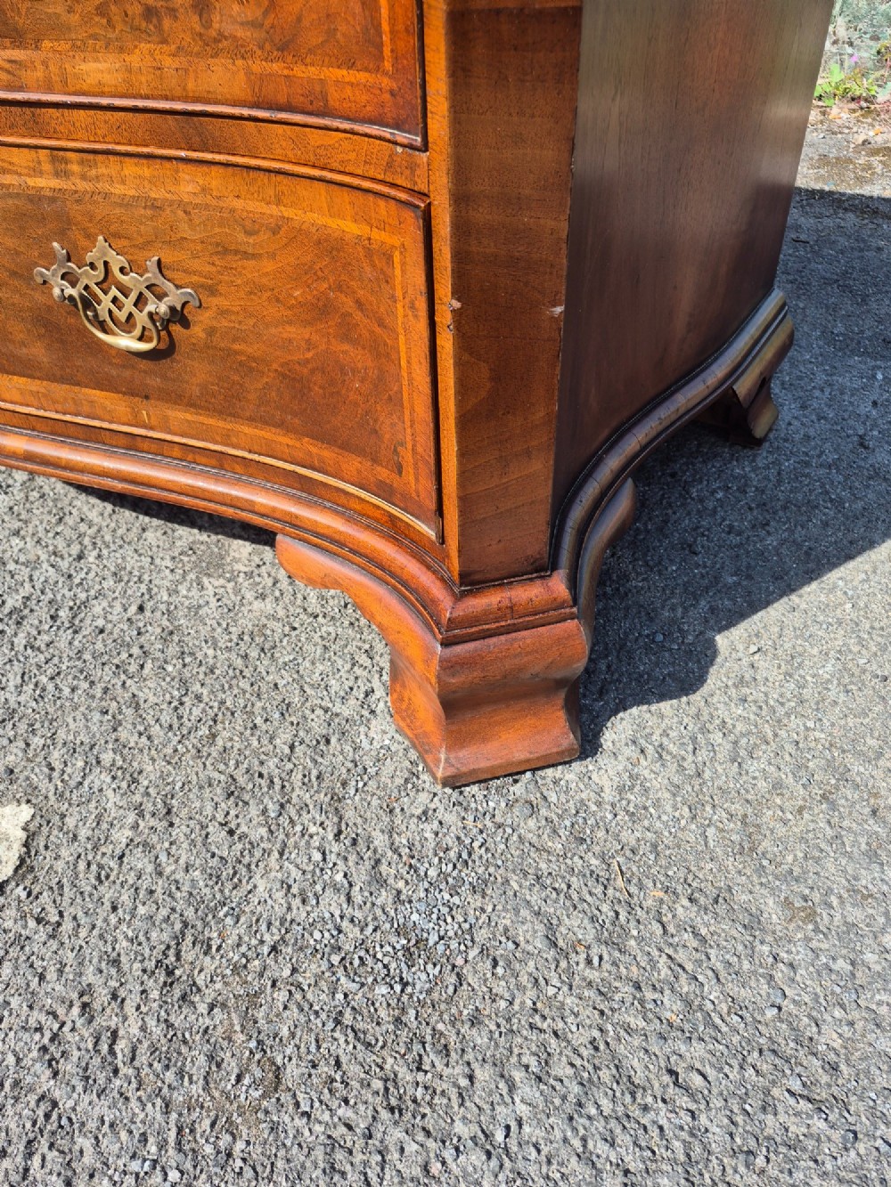 A burr walnut serpentine-front chest of drawers with two short top drawers over three long drawers, featuring brass backplate handles and resting on bracket feet. View XI