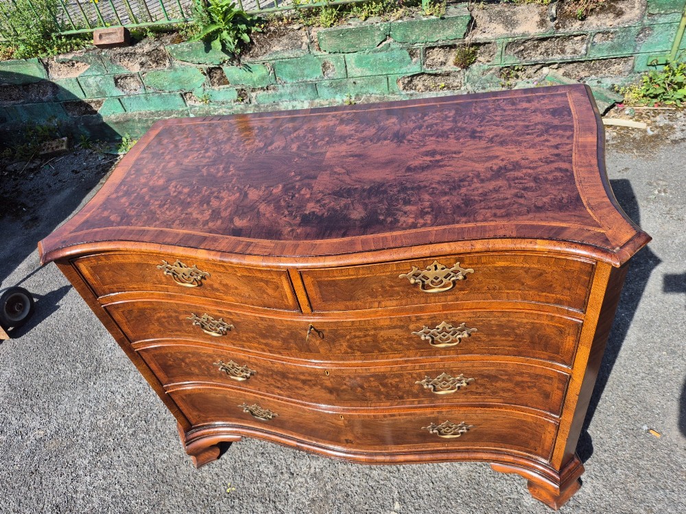 A burr walnut serpentine-front chest of drawers with two short top drawers over three long drawers, featuring brass backplate handles and resting on bracket feet. View XII