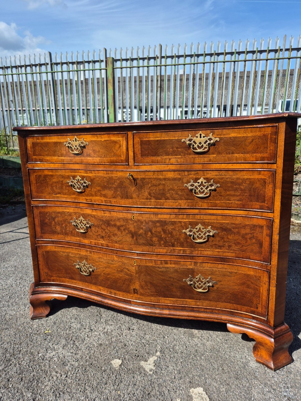 A burr walnut serpentine-front chest of drawers with two short top drawers over three long drawers, featuring brass backplate handles and resting on bracket feet. View XIII