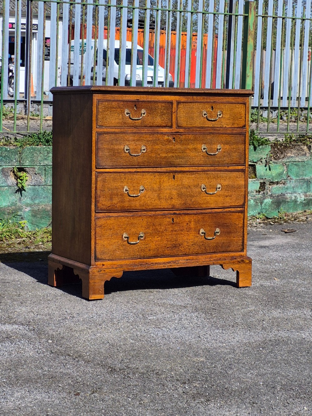 A Georgian golden oak chest of drawers with two short drawers over three long drawers, featuring brass handles and bracket feet.