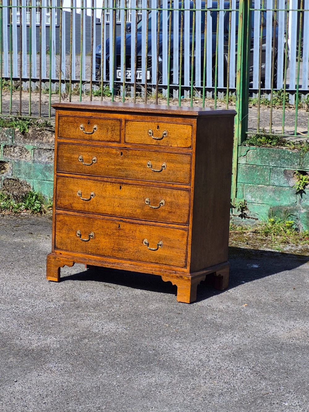 A Georgian golden oak chest of drawers with two short drawers over three long drawers, featuring brass handles and bracket feet. View II