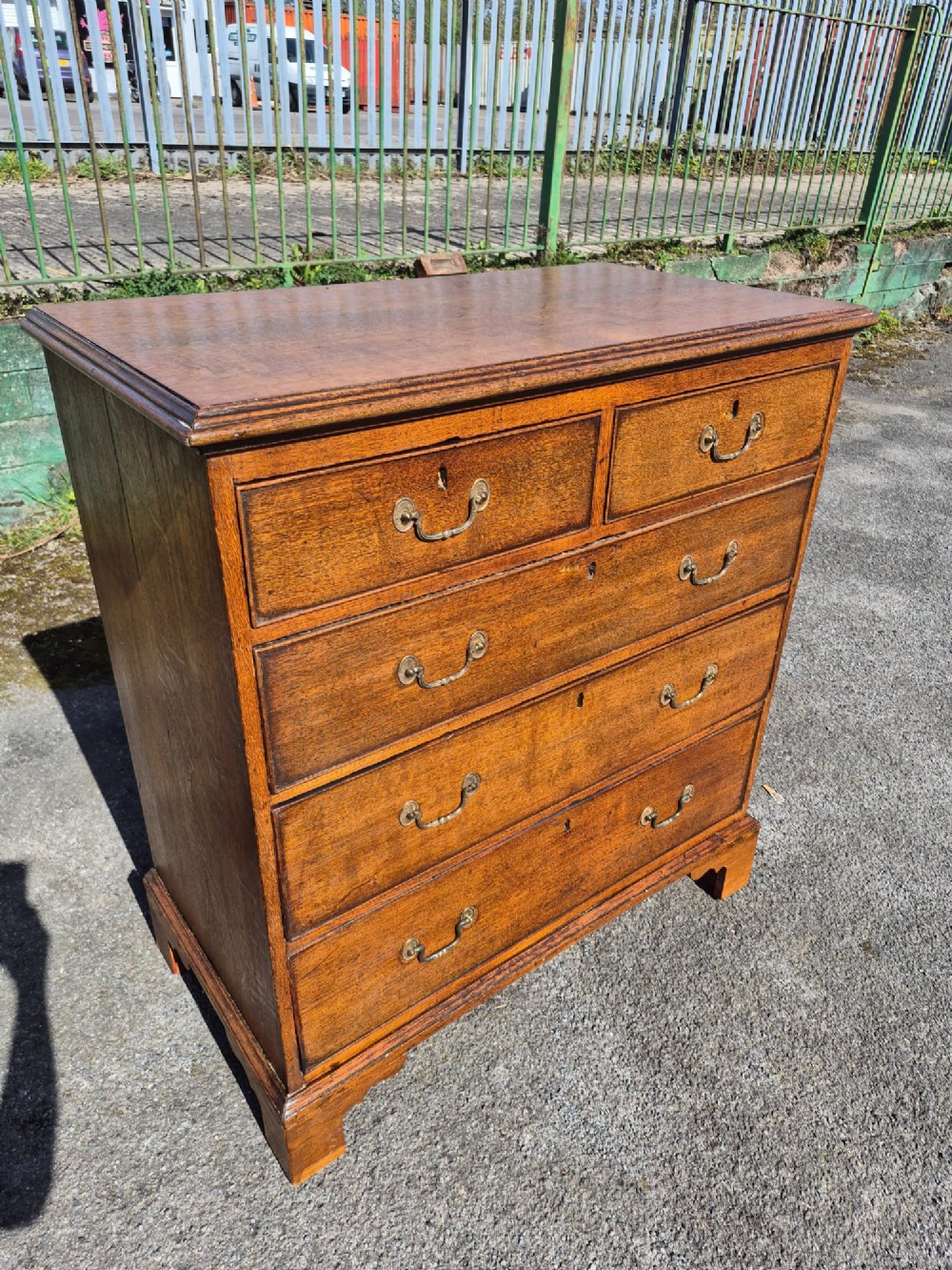 A Georgian golden oak chest of drawers with two short drawers over three long drawers, featuring brass handles and bracket feet. View III