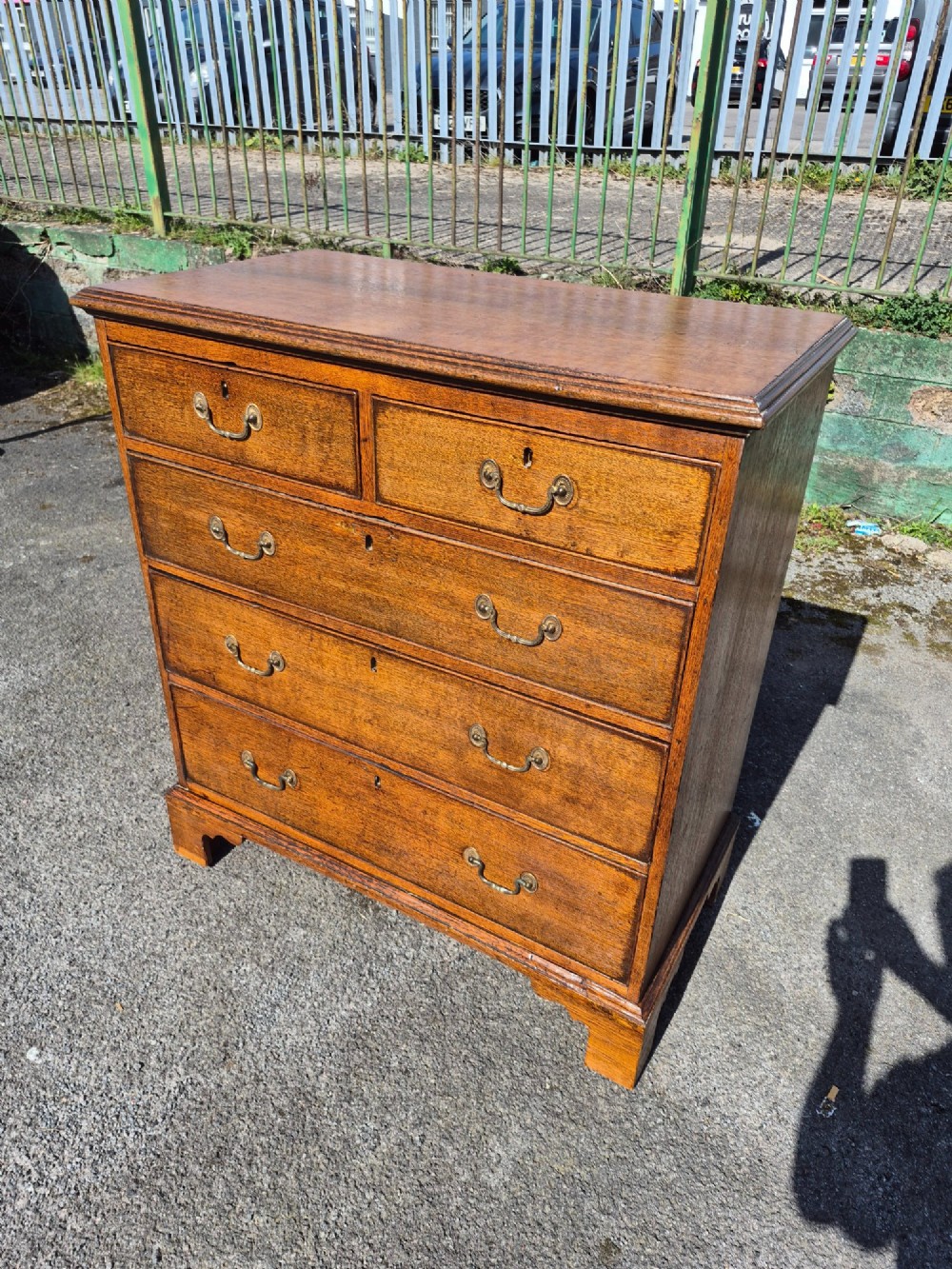 A Georgian golden oak chest of drawers with two short drawers over three long drawers, featuring brass handles and bracket feet. View IV