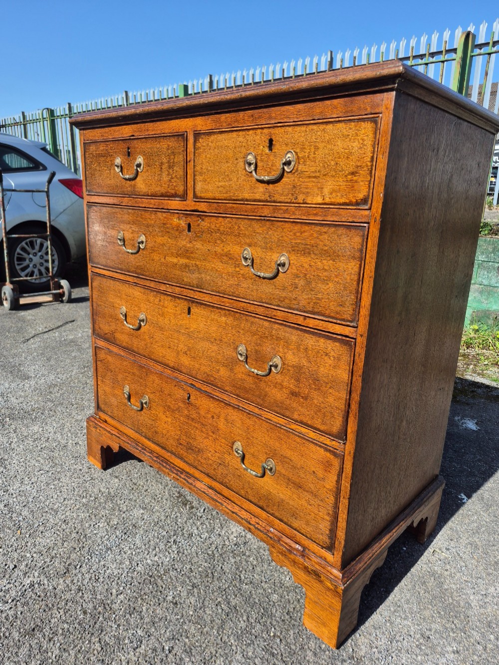 A Georgian golden oak chest of drawers with two short drawers over three long drawers, featuring brass handles and bracket feet. View VI