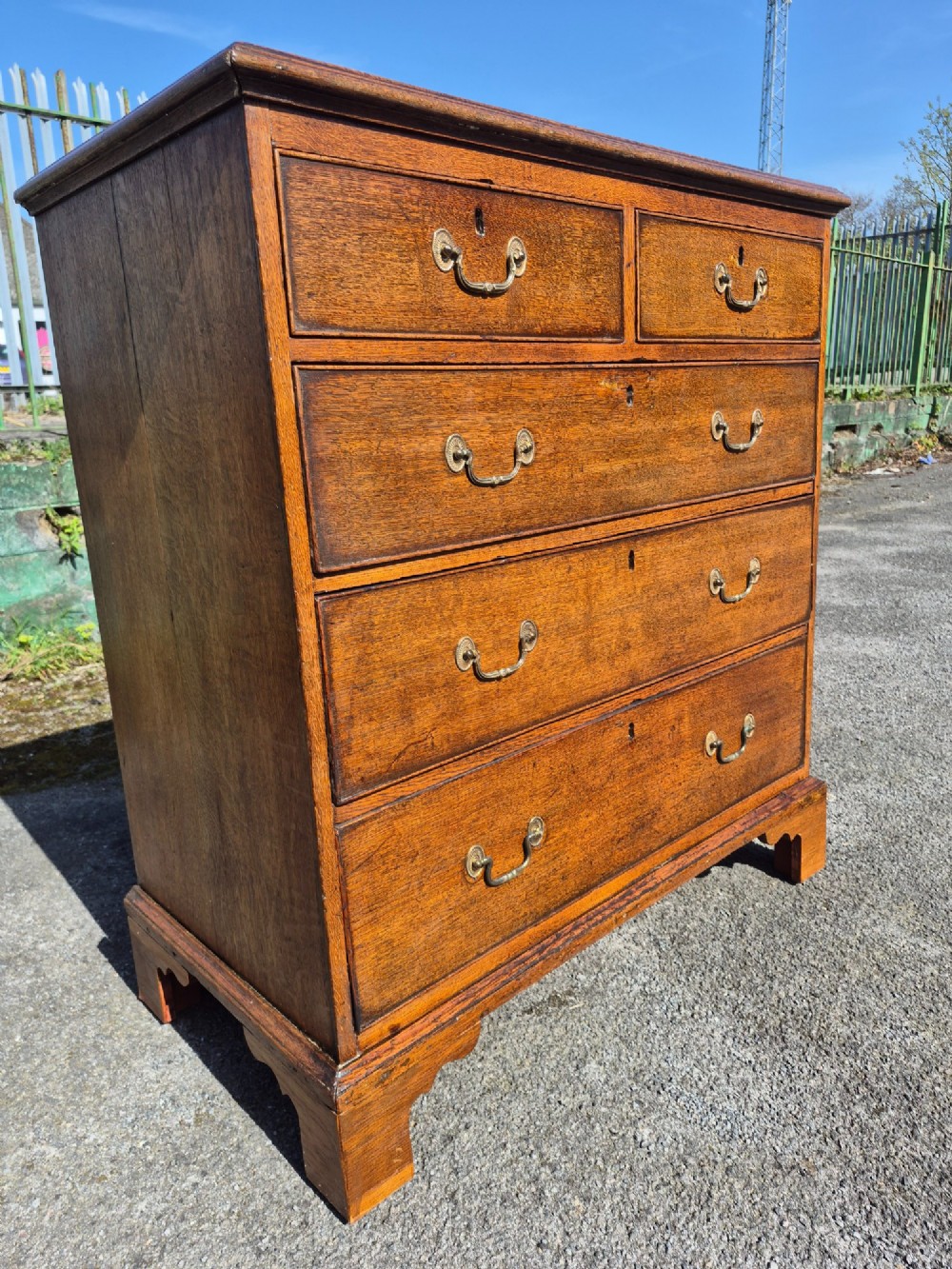 A Georgian golden oak chest of drawers with two short drawers over three long drawers, featuring brass handles and bracket feet. View VII