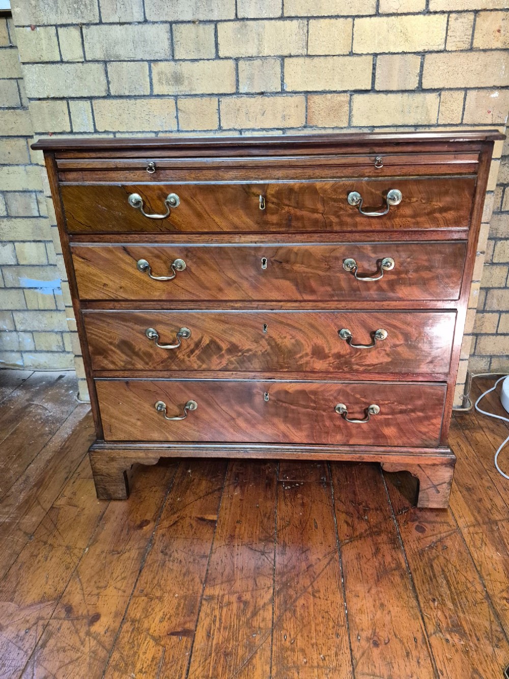 A Georgian mahogany bachelors chest featuring a top brushing slide, four graduated drawers with flame mahogany veneers, brass swan-neck handles, and bracket feet.