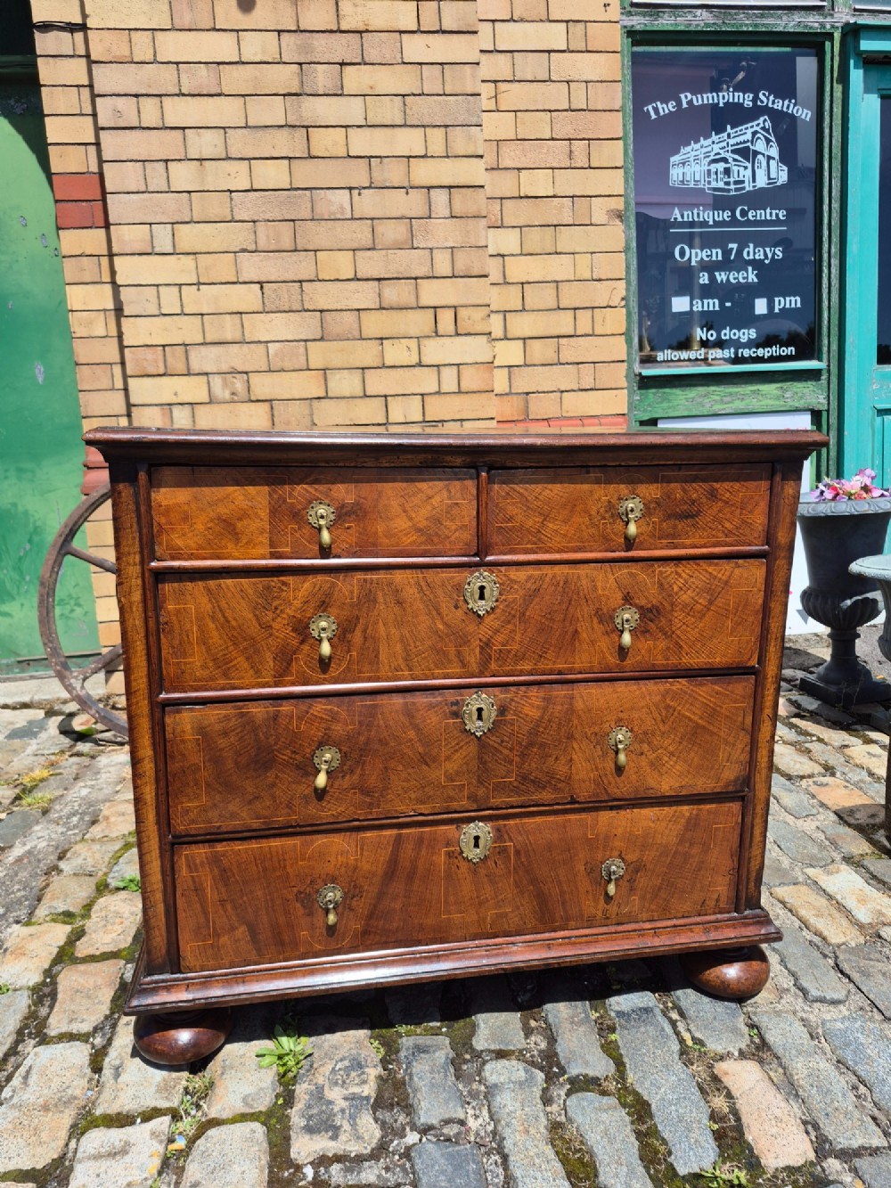 A William and Mary walnut chest of drawers featuring geometric crossbanded drawer fronts, brass drop handles, and compressed bun feet.