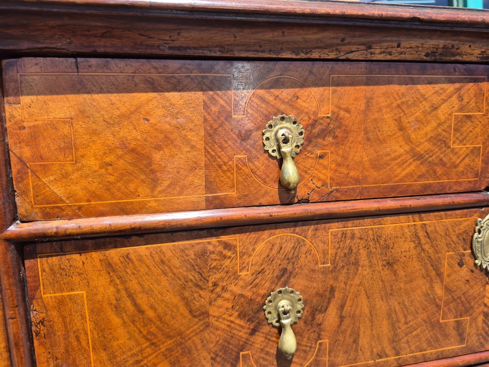 A William and Mary walnut chest of drawers featuring geometric crossbanded drawer fronts, brass drop handles, and compressed bun feet. View X