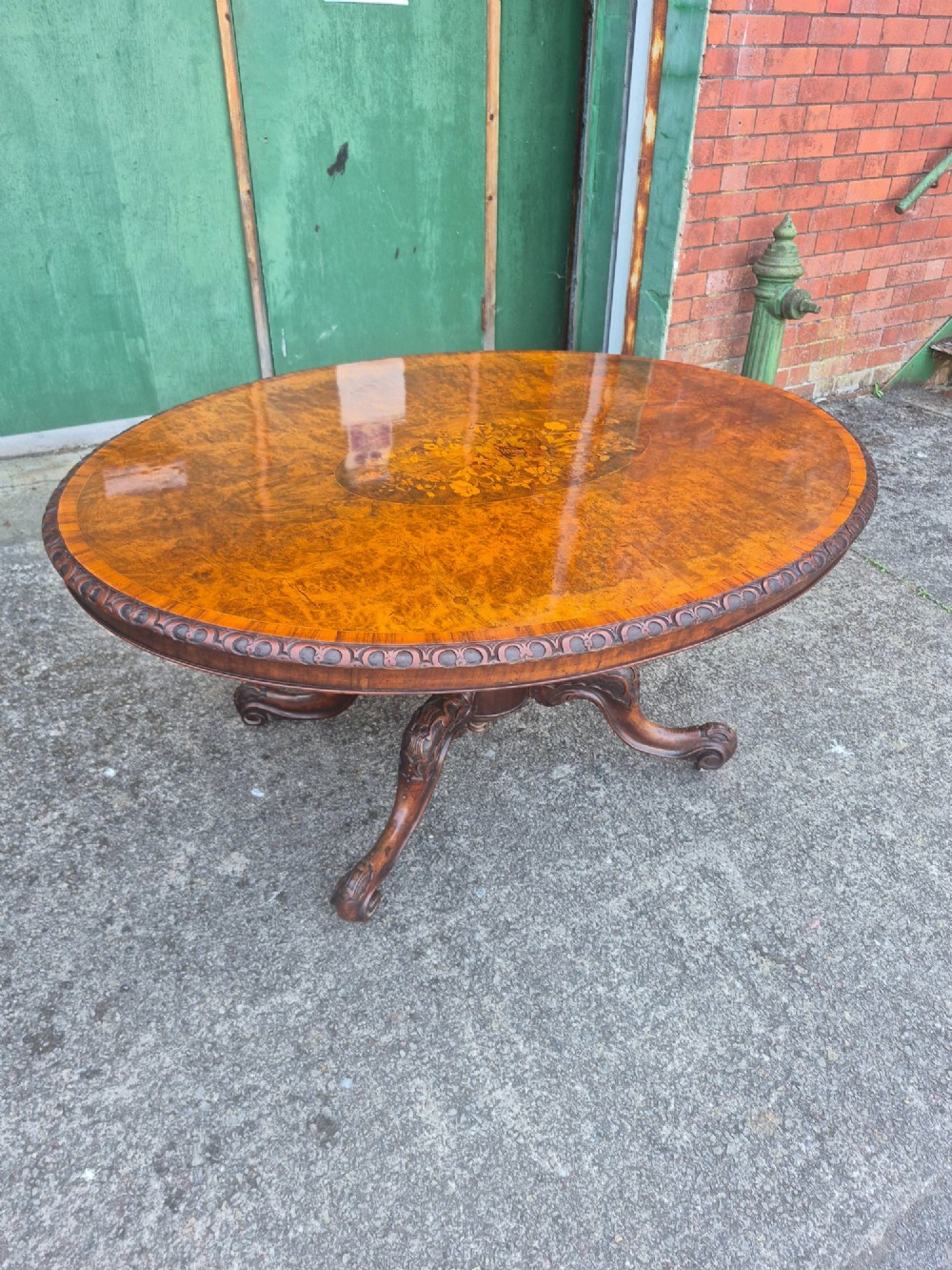 A Victorian oval burr walnut breakfast table with floral marquetry inlay, carved apron, and four carved cabriole legs.