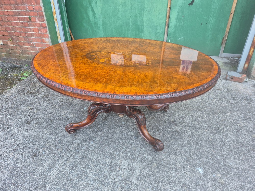 A Victorian oval burr walnut breakfast table with floral marquetry inlay, carved apron, and four carved cabriole legs. View II