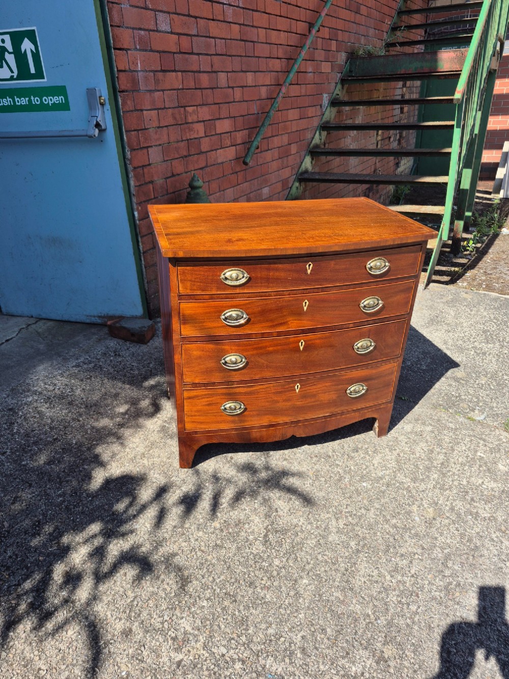 A Regency period mahogany bowfront chest featuring four graduated drawers with oval brass handles and splayed bracket feet.