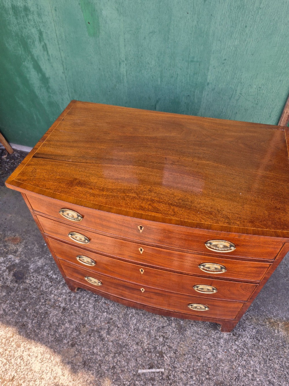 A Regency period mahogany bowfront chest featuring four graduated drawers with oval brass handles and splayed bracket feet. View IV