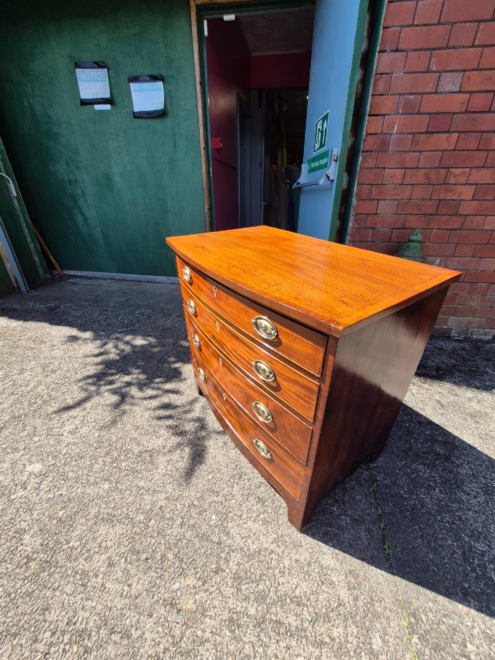 A Regency period mahogany bowfront chest featuring four graduated drawers with oval brass handles and splayed bracket feet. View VII