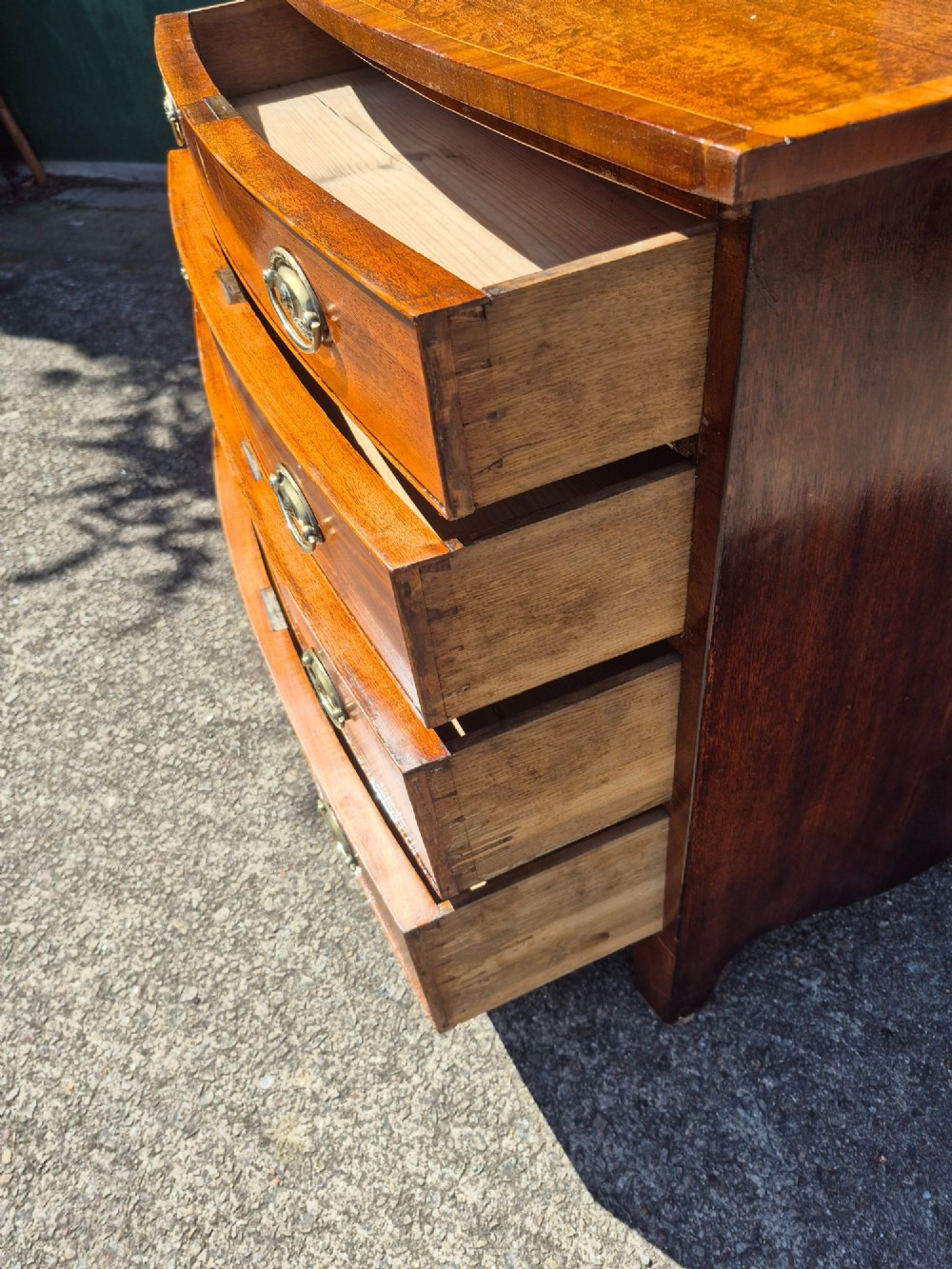 A Regency period mahogany bowfront chest featuring four graduated drawers with oval brass handles and splayed bracket feet. View X