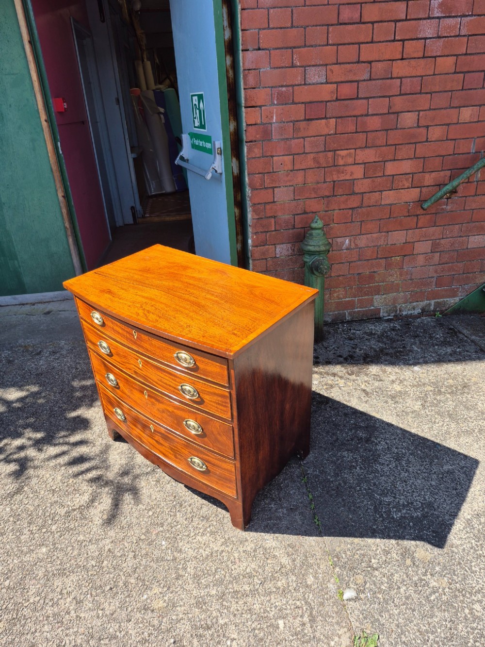 A Regency period mahogany bowfront chest featuring four graduated drawers with oval brass handles and splayed bracket feet. View XI