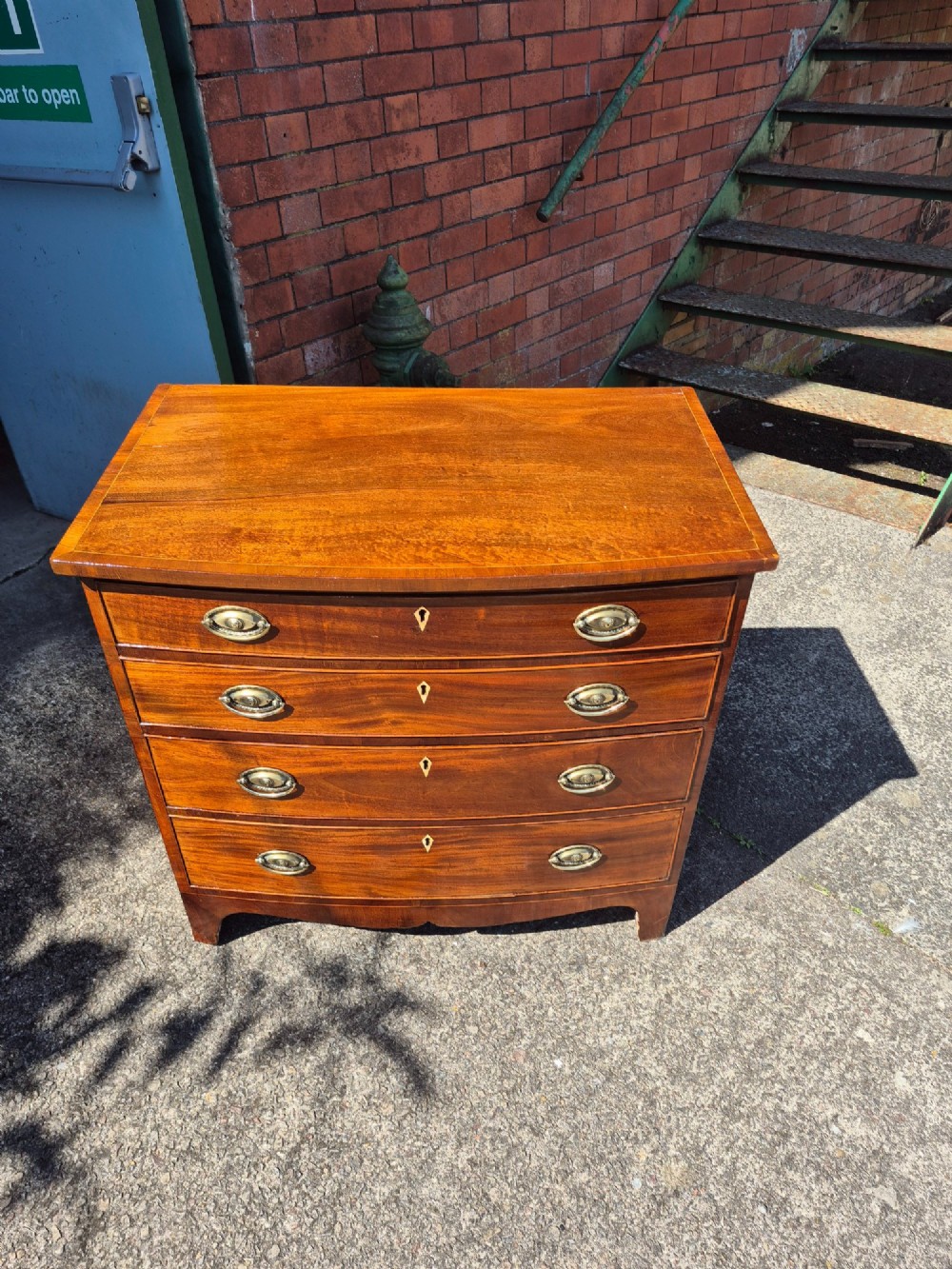 A Regency period mahogany bowfront chest featuring four graduated drawers with oval brass handles and splayed bracket feet. View XII