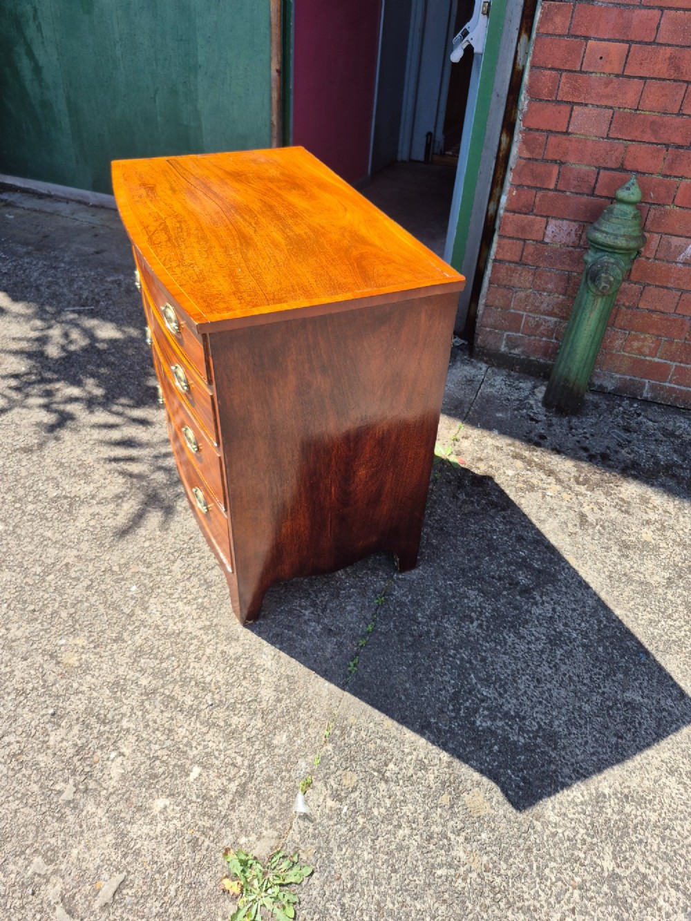 A Regency period mahogany bowfront chest featuring four graduated drawers with oval brass handles and splayed bracket feet. View XV