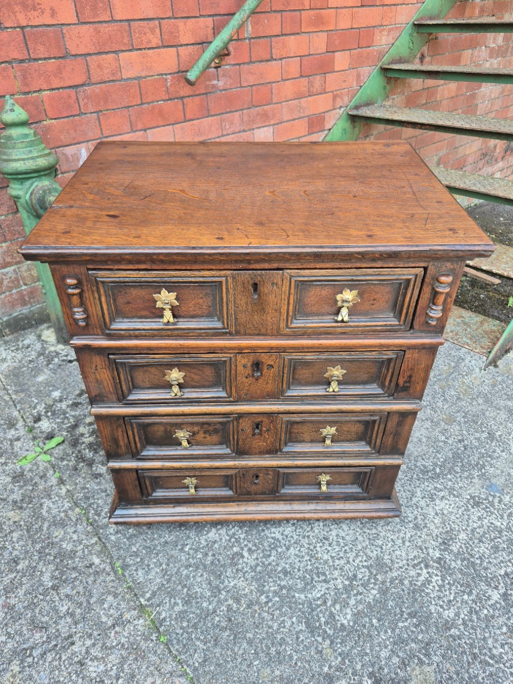 A small antique oak chest featuring four drawers with geometric moulding panels and brass drop handles.
