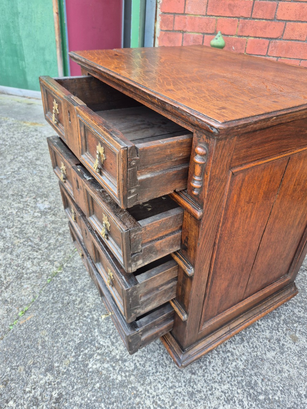 A small antique oak chest featuring four drawers with geometric moulding panels and brass drop handles. View IV