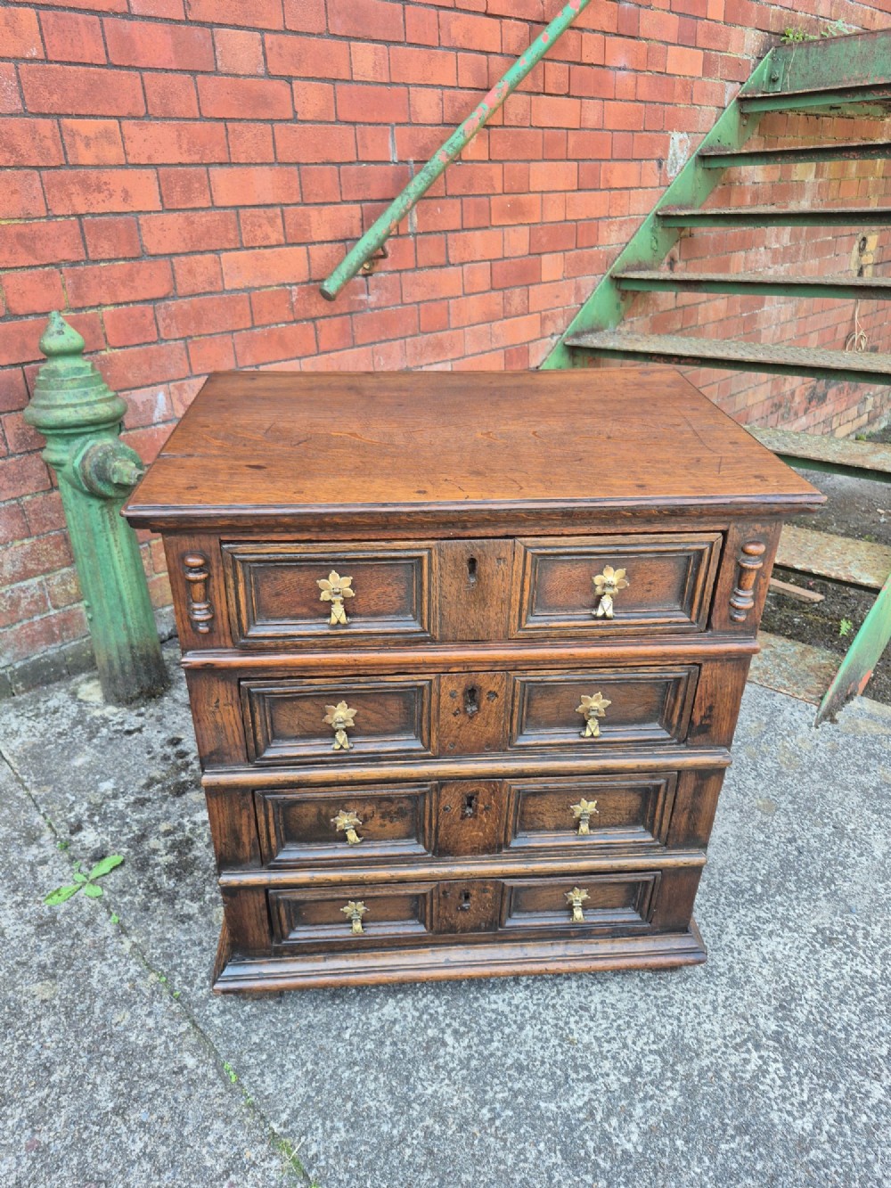 A small antique oak chest featuring four drawers with geometric moulding panels and brass drop handles. View VIII
