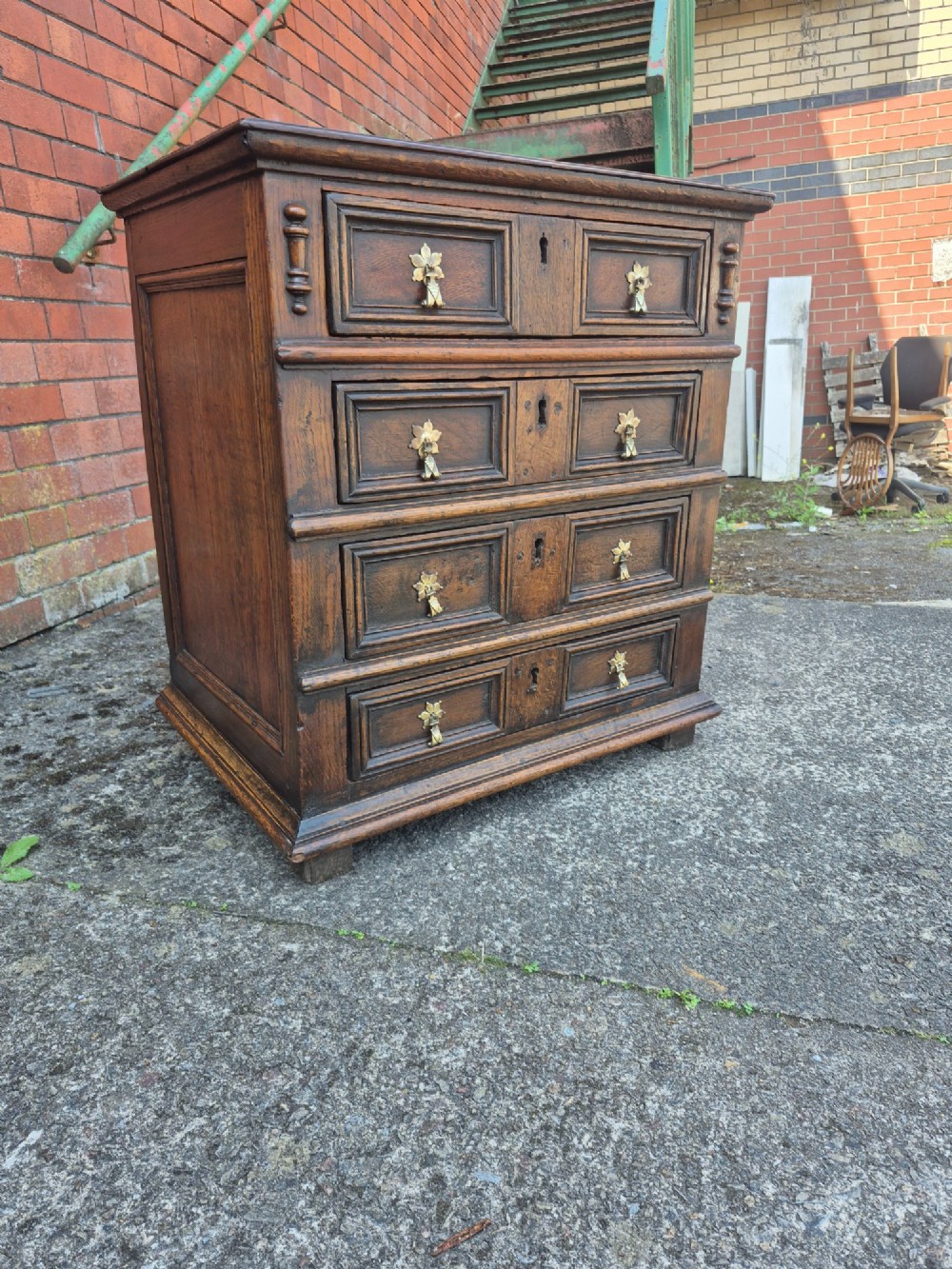 A small antique oak chest featuring four drawers with geometric moulding panels and brass drop handles. View IX