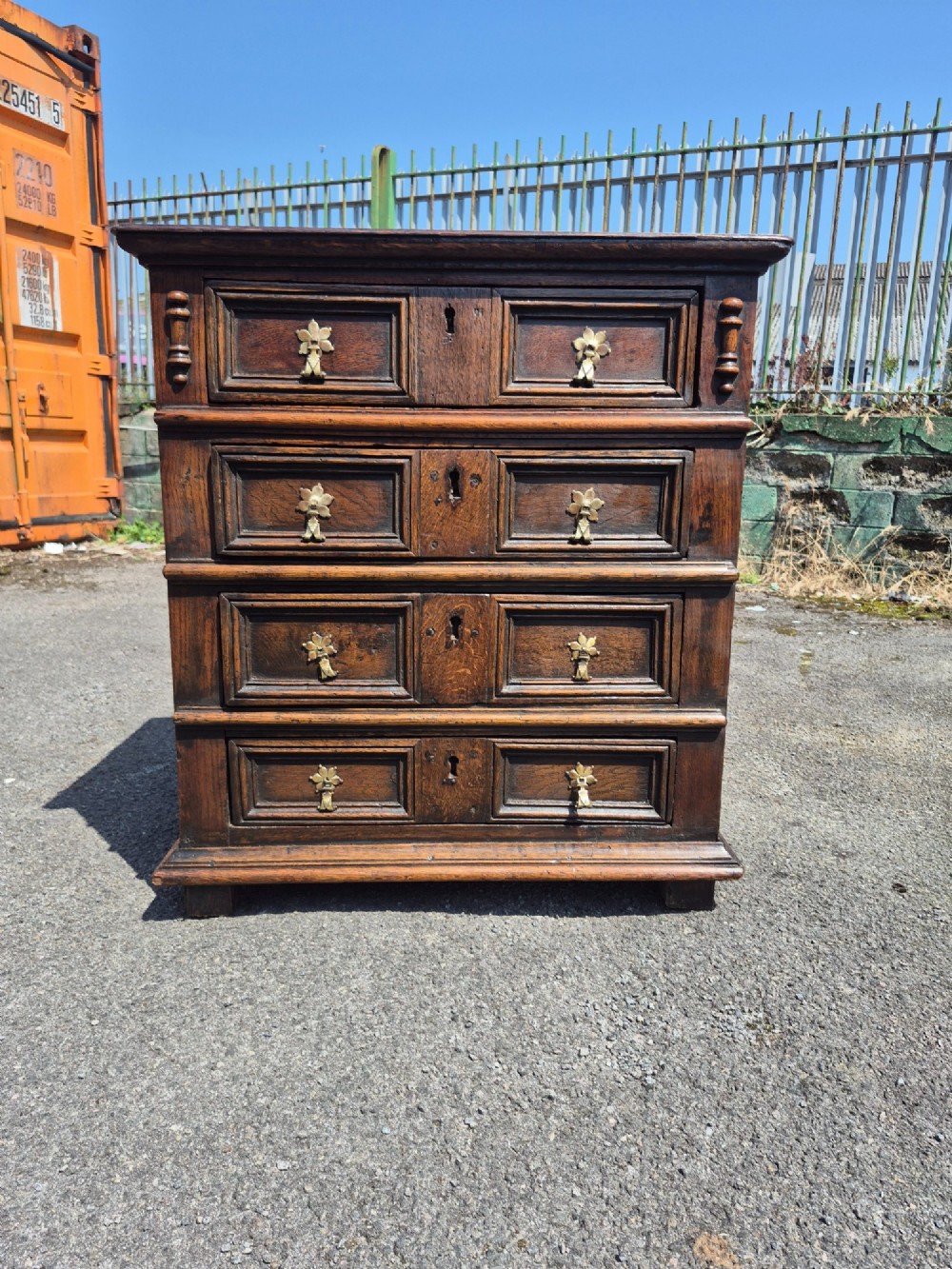 A small antique oak chest featuring four drawers with geometric moulding panels and brass drop handles. View X