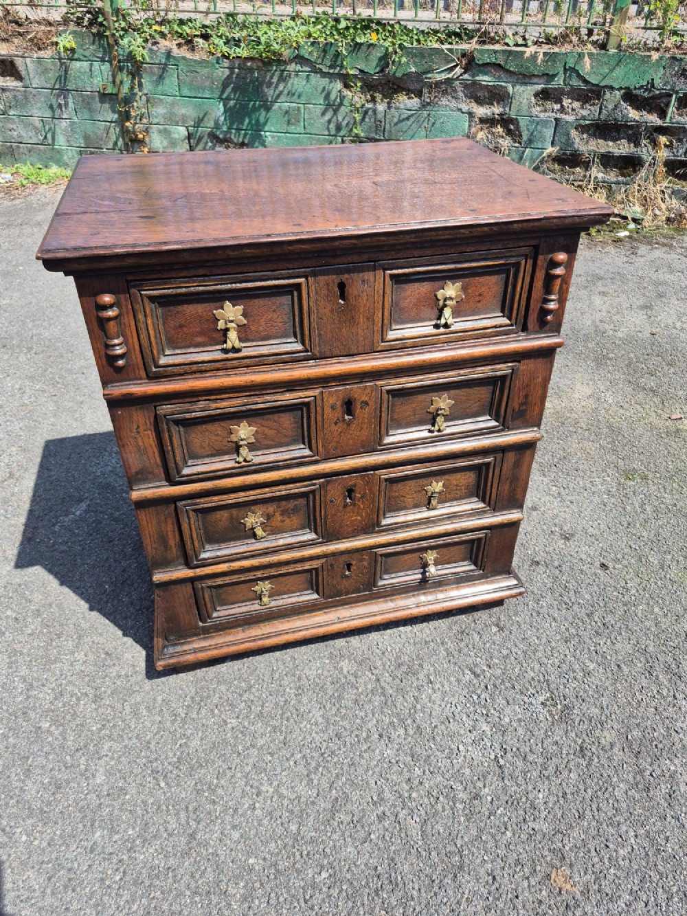 A small antique oak chest featuring four drawers with geometric moulding panels and brass drop handles. View XI