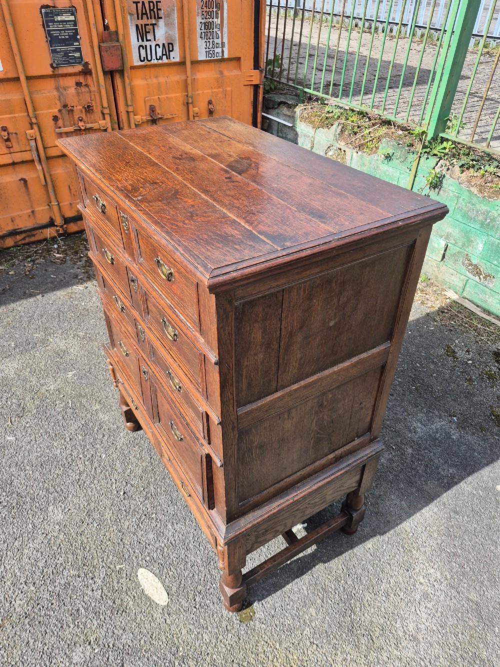 A 17th-century Charles II dark oak chest on stand featuring geometric panel mouldings, brass drop handles, and turned legs with connecting stretchers. View II
