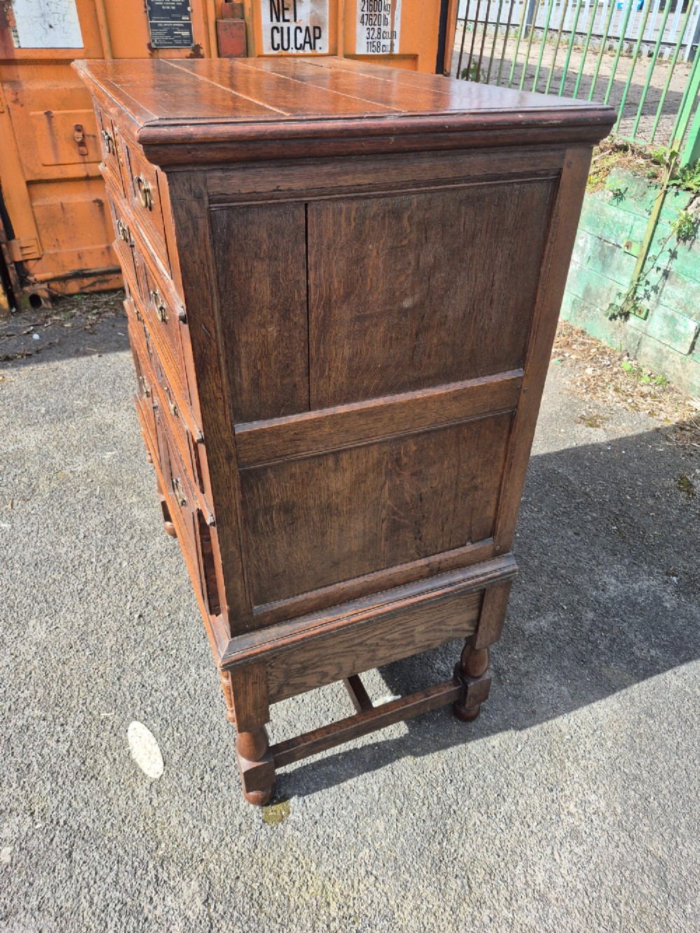 A 17th-century Charles II dark oak chest on stand featuring geometric panel mouldings, brass drop handles, and turned legs with connecting stretchers. View III