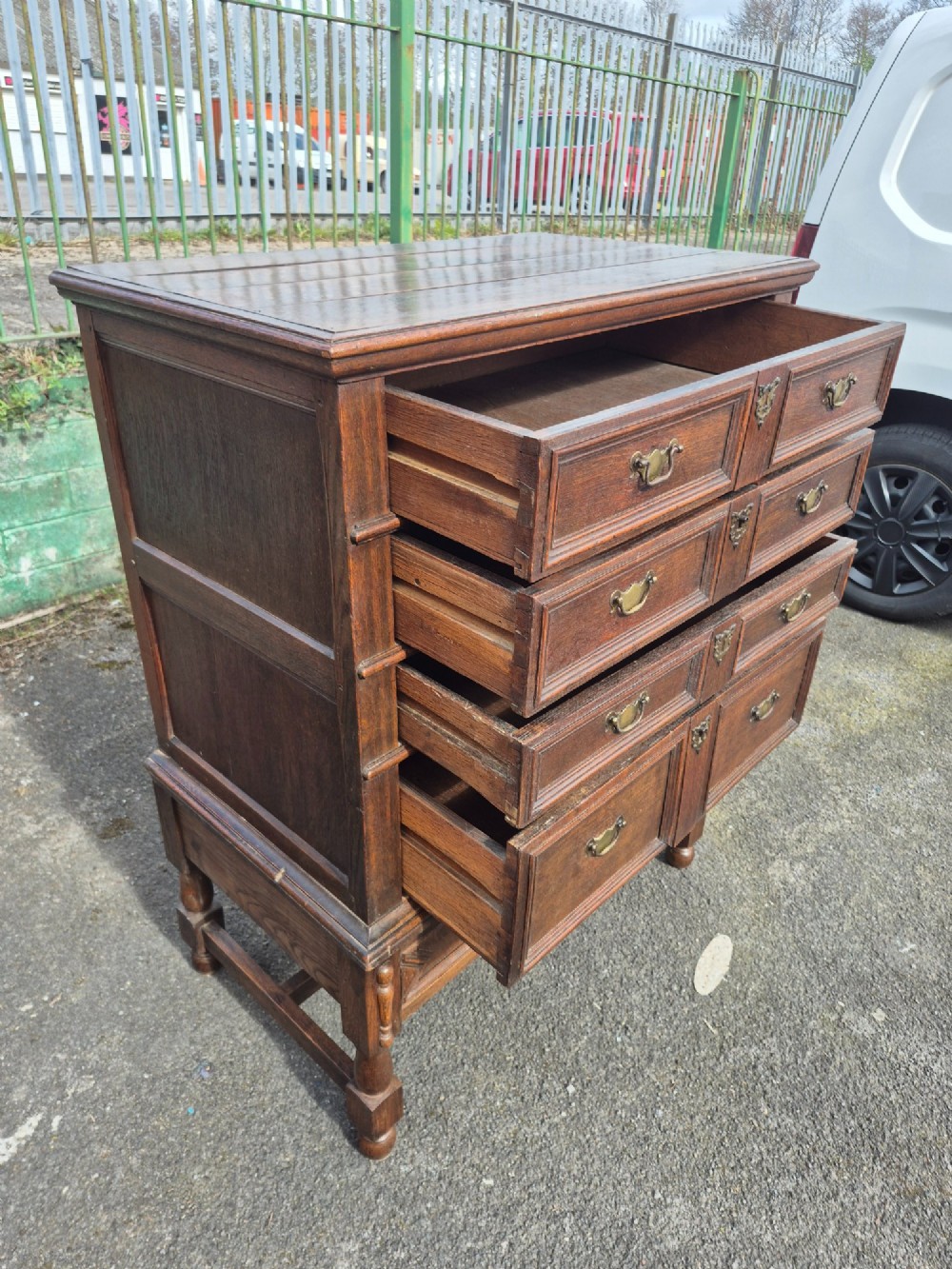 A 17th-century Charles II dark oak chest on stand featuring geometric panel mouldings, brass drop handles, and turned legs with connecting stretchers. View VI
