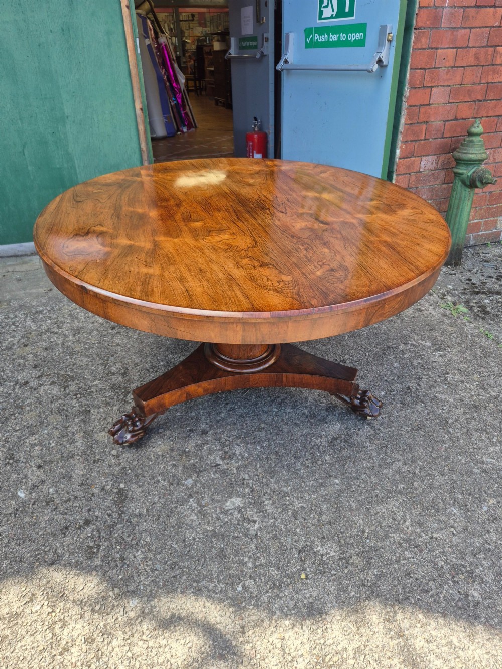 A circular Regency rosewood breakfast table featuring a figured veneer top resting on a central pedestal column with a triform base and carved feet. View II