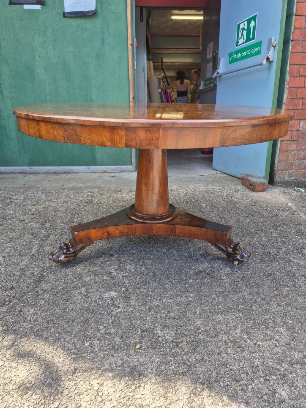 A circular Regency rosewood breakfast table featuring a figured veneer top resting on a central pedestal column with a triform base and carved feet. View III
