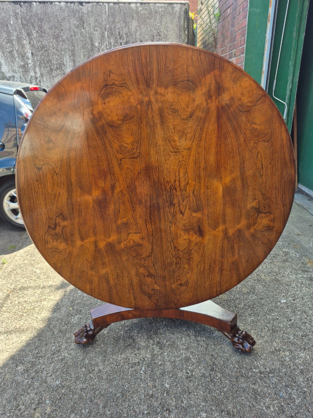 A circular Regency rosewood breakfast table featuring a figured veneer top resting on a central pedestal column with a triform base and carved feet. View V