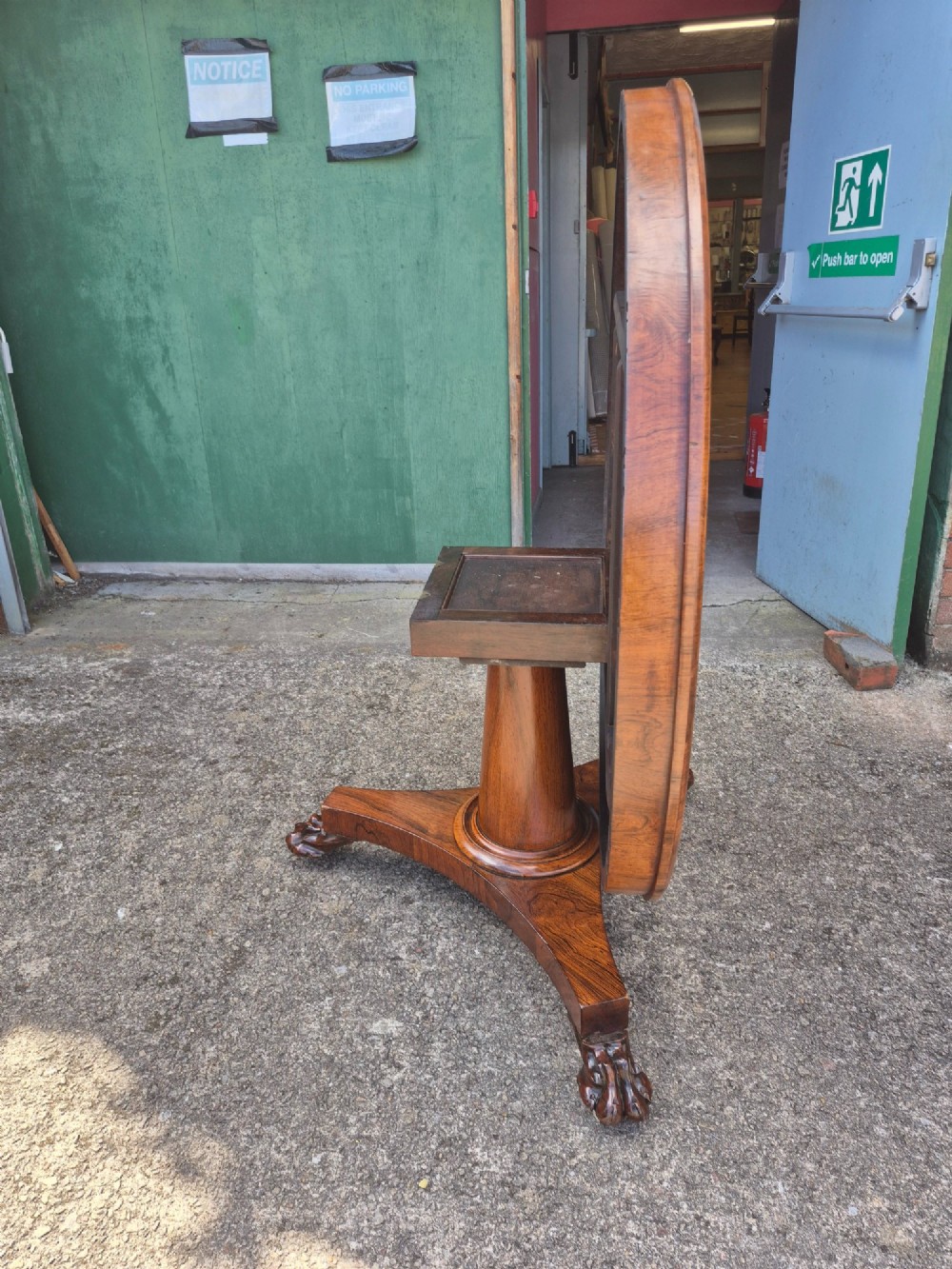 A circular Regency rosewood breakfast table featuring a figured veneer top resting on a central pedestal column with a triform base and carved feet. View VI