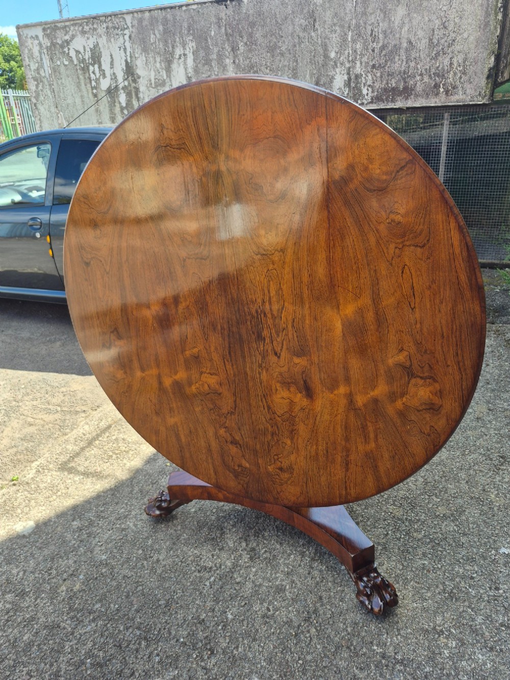 A circular Regency rosewood breakfast table featuring a figured veneer top resting on a central pedestal column with a triform base and carved feet. View VII