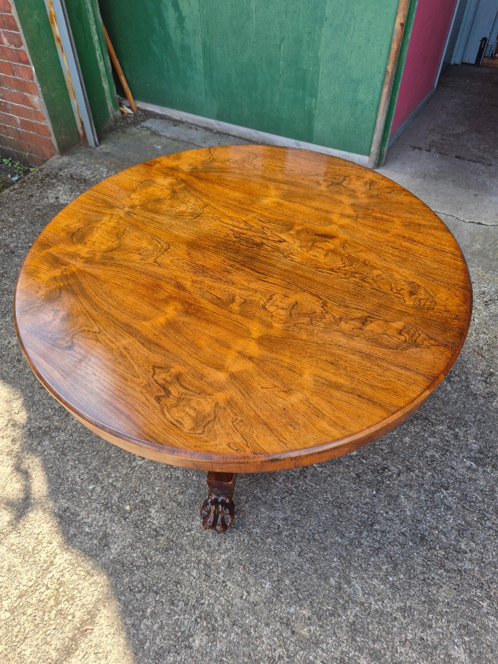 A circular Regency rosewood breakfast table featuring a figured veneer top resting on a central pedestal column with a triform base and carved feet. View IX