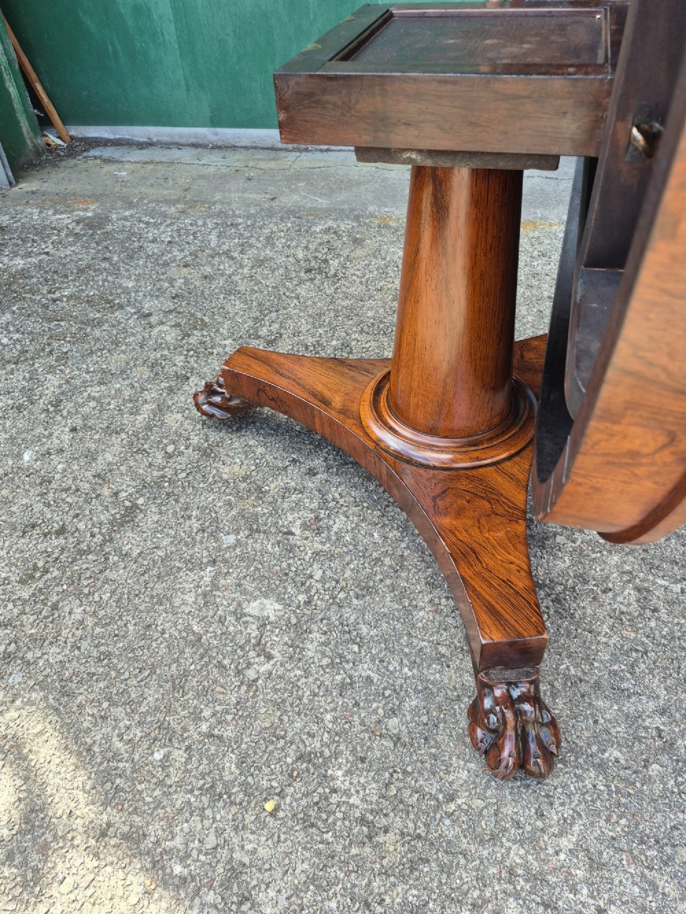 A circular Regency rosewood breakfast table featuring a figured veneer top resting on a central pedestal column with a triform base and carved feet. View X
